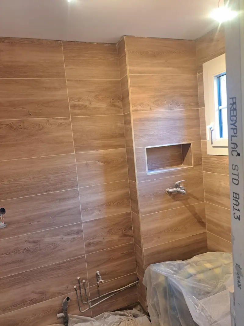 Salle de bain en cours : carrelage effet bois posé, niche encastrée, plomberie en attente