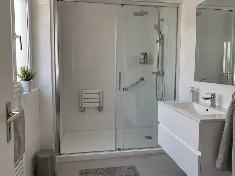 Ancienne place de baignoire transformée en douche avec porte coulissante, siège rabattable et barre d'appui